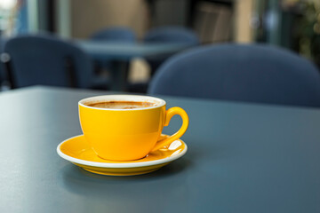 A cup of black coffee americano in a yellow cup in a cafe with copy space
