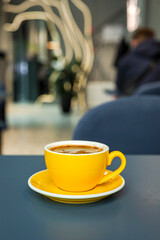 A cup of black coffee americano in a yellow cup in a cafe with copy space
