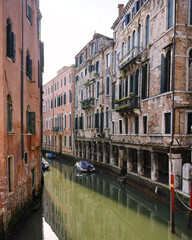Narrow canal with old Venetian buildings and calm water in Venice Italy on summer day
