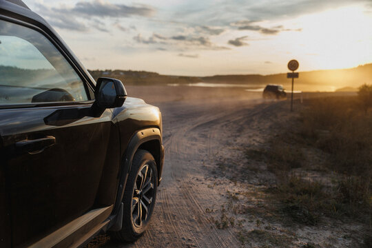 A car is parked on the side of a dirt road during sunset hours
