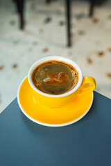 A cup of black coffee americano in a yellow cup in a cafe with copy space
