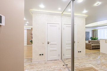 A well-lit interior features marble flooring, white doors, and a large mirror reflecting the space. A cozy living room is visible beyond an opening