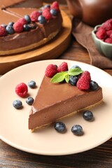 Piece of tasty chocolate cheesecake with berries on wooden table, closeup