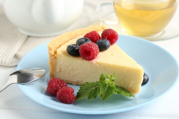 Piece of delicious cheesecake with fresh berries and mint served on white wooden table, closeup