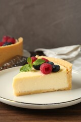Piece of delicious cheesecake with fresh berries and mint on wooden table, closeup