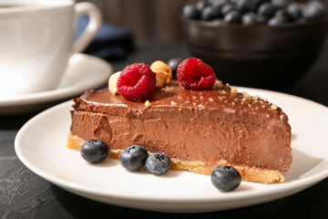 Piece of delicious chocolate cheesecake with nuts and berries on black table, closeup