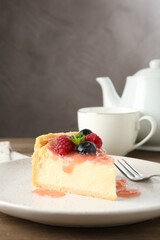Piece of tasty cheesecake with berries and sauce served on wooden table, closeup