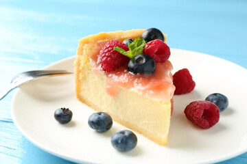 Piece of tasty cheesecake with berries and sauce on light blue wooden table, closeup