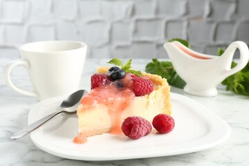 Piece of tasty cheesecake with berries and sauce served on white marble table, closeup
