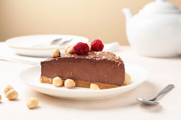 Piece of delicious chocolate cheesecake with nuts and raspberries on beige table, closeup