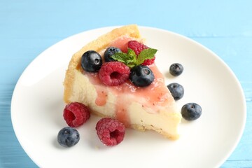 Piece of tasty cheesecake with berries and sauce on light blue wooden table, closeup