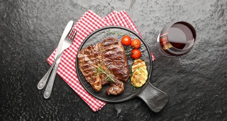 Delicious grilled beef steak with rosemary, zucchini and tomatoes served on dark textured table, flat lay