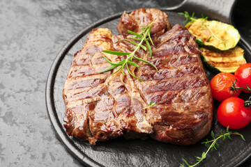 Delicious grilled beef steak with rosemary, zucchini and tomatoes on dark textured table, closeup