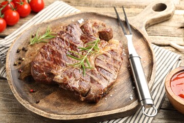 Delicious grilled beef steak with rosemary, spices, carving fork and ketchup on wooden table, closeup