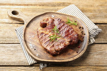 Delicious grilled beef steak with rosemary, salt and peppercorns on wooden table, closeup