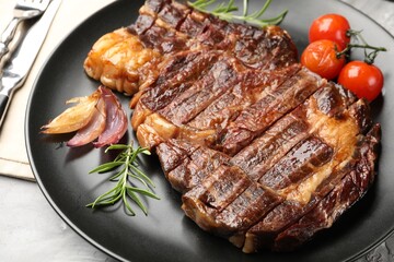 Delicious grilled beef steak with rosemary, onion and tomatoes on grey textured table, closeup