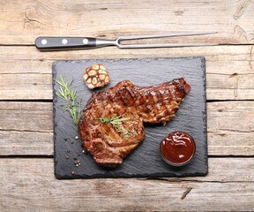 Delicious grilled beef steak with herbs, spices, carving fork and ketchup on wooden table, flat lay