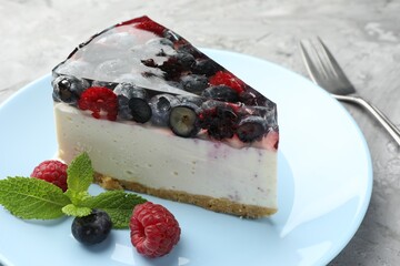 Piece of delicious cheesecake with berries, mint and fork on grey table, closeup