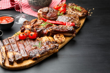 Pieces of tasty grilled beef with rosemary and vegetables on black wooden table, space for text