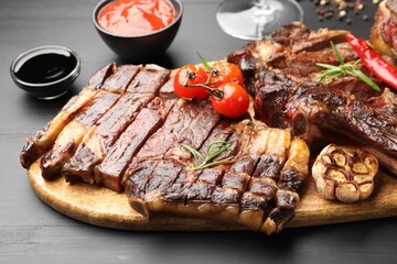 Pieces of tasty grilled beef with rosemary and vegetables on black wooden table, closeup