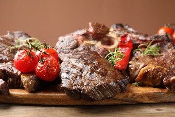 Pieces of tasty grilled beef with rosemary and vegetables on wooden table, closeup