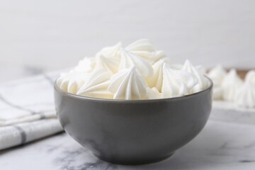 Delicious meringue cookies in bowl on white marble table, closeup