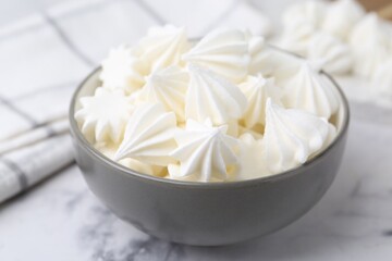 Delicious meringue cookies in bowl on white marble table, closeup