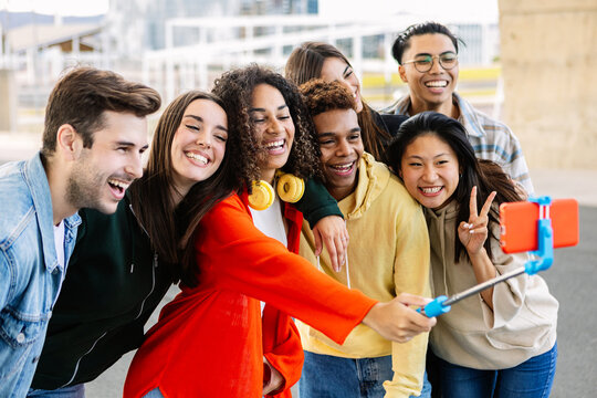 Multiracial group of young students smiling and taking a selfie with a smartphone on a selfie stick