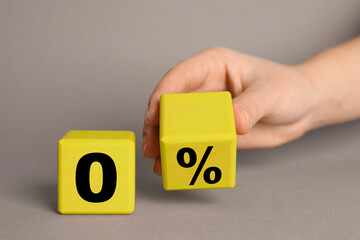 Zero commission. Woman putting yellow cube with percent sign next to another one with 0 on grey background, closeup