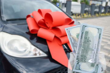 Dollars in jar against car with red bow outdoors. Save money for vehicle