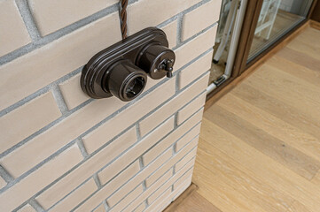 Vintage-style dark brown switch and outlet on a light brick wall with wood flooring