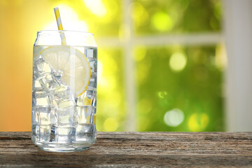 Refreshing water with lemon and ice on table against window in room. Space for text