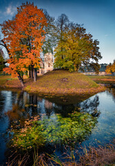 Attractive morning view of Palace Olszanica on the shore of small river. Impressive autumn cityscape of Olszanica town, Poland, Europe. Trees covered with orange and crimson leaves.