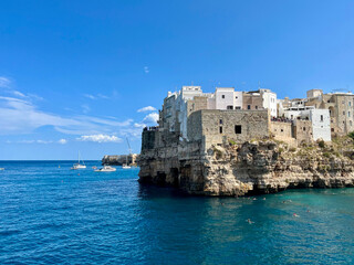 Polignano a Mare an der Adriak&uuml;ste in Apulien, Italien. Historische Altstadt auf hohen Felsen &uuml;ber dem t&uuml;rkisblauen Meer, Boote und Schwimmer im klaren Wasser an einem sonnigen Tag.
