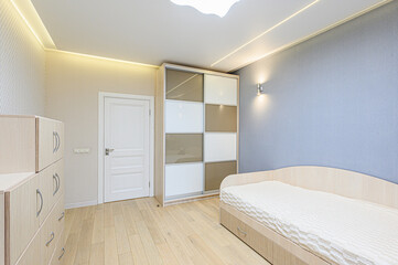 A neat bedroom with light wood floors, a white door, a sliding door wardrobe, and a bed. Soft lighting enhances the serene ambiance