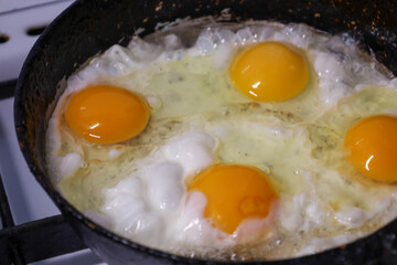 This appetizing close-up shows four bright egg yolks and cooking egg white in an old, hot frying pan. It is a perfect shot to illustrate themes of breakfast, simple cooking, home cuisine, and concepts