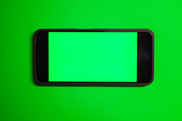 A smartphone with a green screen in horizontal orientation rests on a saturated green background, creating a monochromatic look.