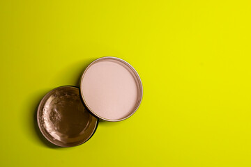 A round metal tin and its lid rest on a bright yellow (lime) background, creating a minimalist shot with strong color contrast. The light contents of the container and the shiny inside of the lid add 