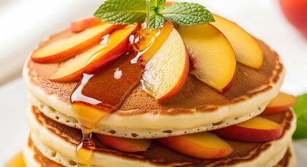 A stack of golden brown pancakes is generously topped with sliced fresh peaches and drizzled with syrup, garnished with mint, isolated on white background