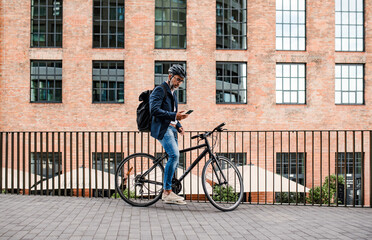 Fototapeta premium City commuter riding bike from work, reading text message on phone.