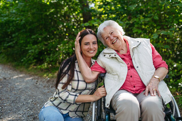 Mature daughter taking senior mother in wheelchair on walk in nature.