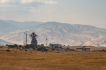 Abandoned and unfinished radio telescope complex standing on a dry plateau surrounded by mountains and grassland under cloudy sky