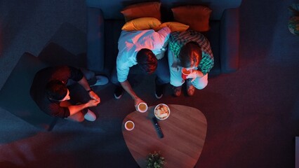 Happy family and colleague sitting at dark living room with red filter while cheering football team...