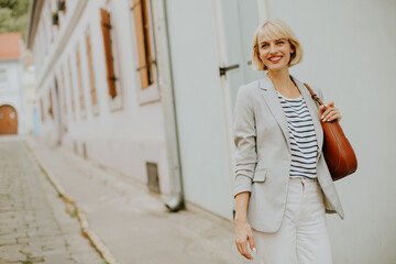 Smiling woman walking down a narrow street in a European town wearing a striped shirt and light blazer
