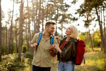 Happy couple enjoys a sunny hike in the forest with backpacks during early evening