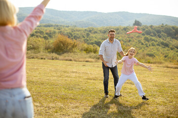 Family enjoys a sunny afternoon playing catch in a grassy field surrounded by mountains in early autumn