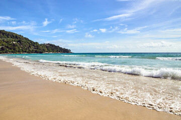 Sunny beach with gentle waves and clear blue sky capturing serene seaside landscape.
