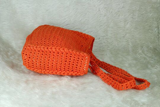 Crocheted handmade orange bag on furry white blanket.