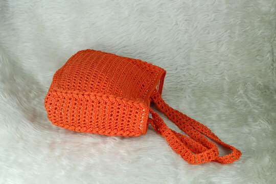 Crocheted handmade orange bag on furry white blanket.