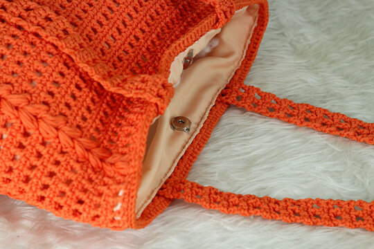 Crocheted handmade orange bag on furry white blanket.